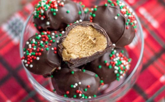 buckeyes with red and green sprinkles, in a clear bowl on a plaid tablecloth