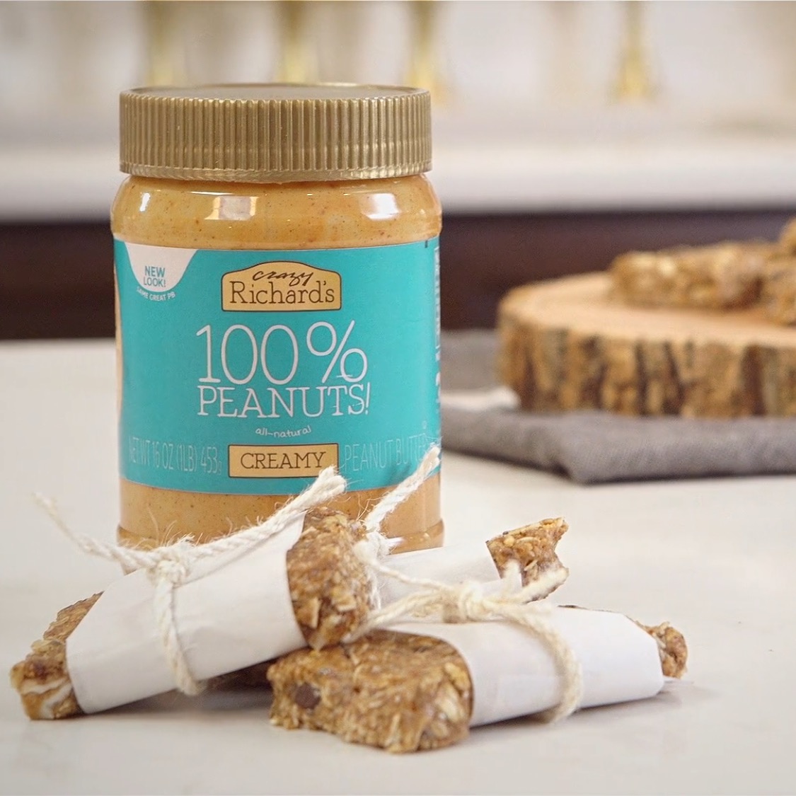 homemade granola bars wrapped in parchment paper tied with string, in front of a jar of Crazy Richard's creamy peanut butter