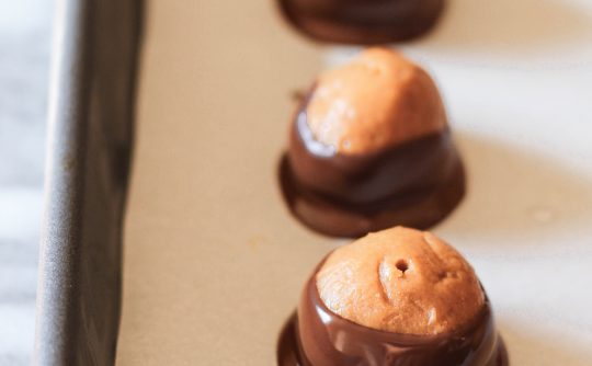 peanut butter balls dipped in chocolate lined up in a row on a parchment-lined baking sheet