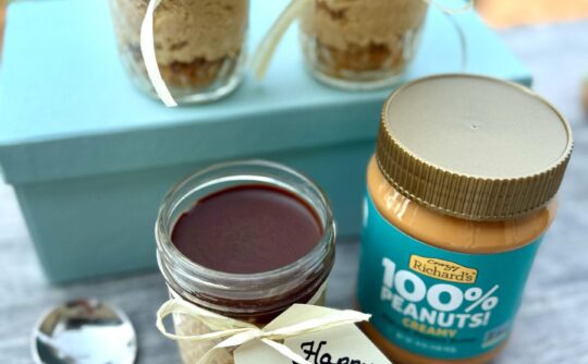 Photo of three jars of chocolate peanut butter cheesecake desserts, alongside a spoon and a jar of Crazy Richard's 100% Peanuts Creamy Peanut butter. One of the jars has a gift tag attached to the jar with a ribbon. The tag says "Happy Father's Day!"