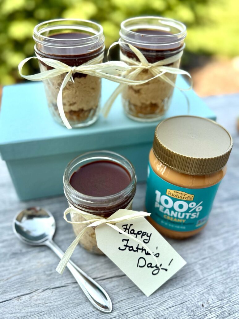 Photo of three jars of chocolate peanut butter cheesecake desserts, alongside a spoon and a jar of Crazy Richard's 100% Peanuts Creamy Peanut butter. One of the jars has a gift tag attached to the jar with a ribbon. The tag says "Happy Father's Day!"
