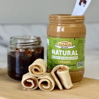 photo of a jar of Crazy Richards Natural No Stir Peanut butter, a jar of homemade jelly, and PB&J Sushi bites arranged on a wooden cutting board.