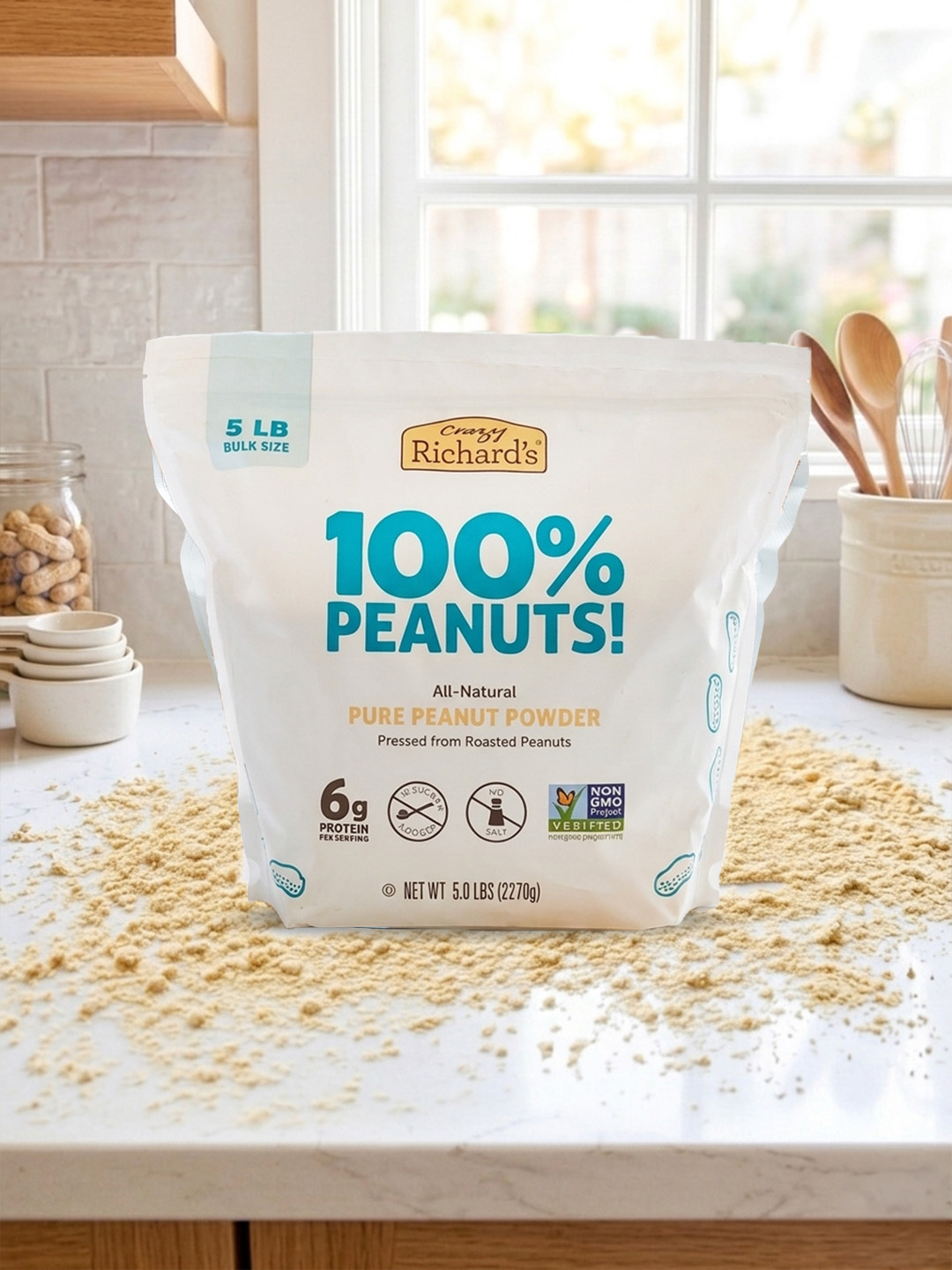 image of a 5-lb bag of Crazy Richard's 100% Peanuts Pure Peanut Powder sitting on a white kitchen countertop, with peanut powder artfully scattered around the bag.