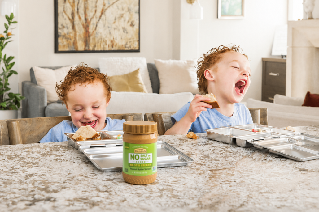 photo of twin boys about 4-5 years old laughing while eating peanut butter sandwiches made with Crazy Richard's Natural No-Stir peanut butter