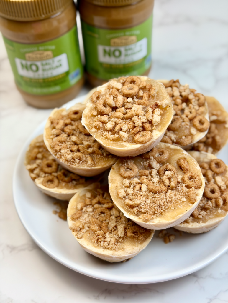 Apple cinnamon peanut butter ice cream cups stacked onto a plate. Behind are two jars of Crazy Richard's Natural No-Stir Peanut butter