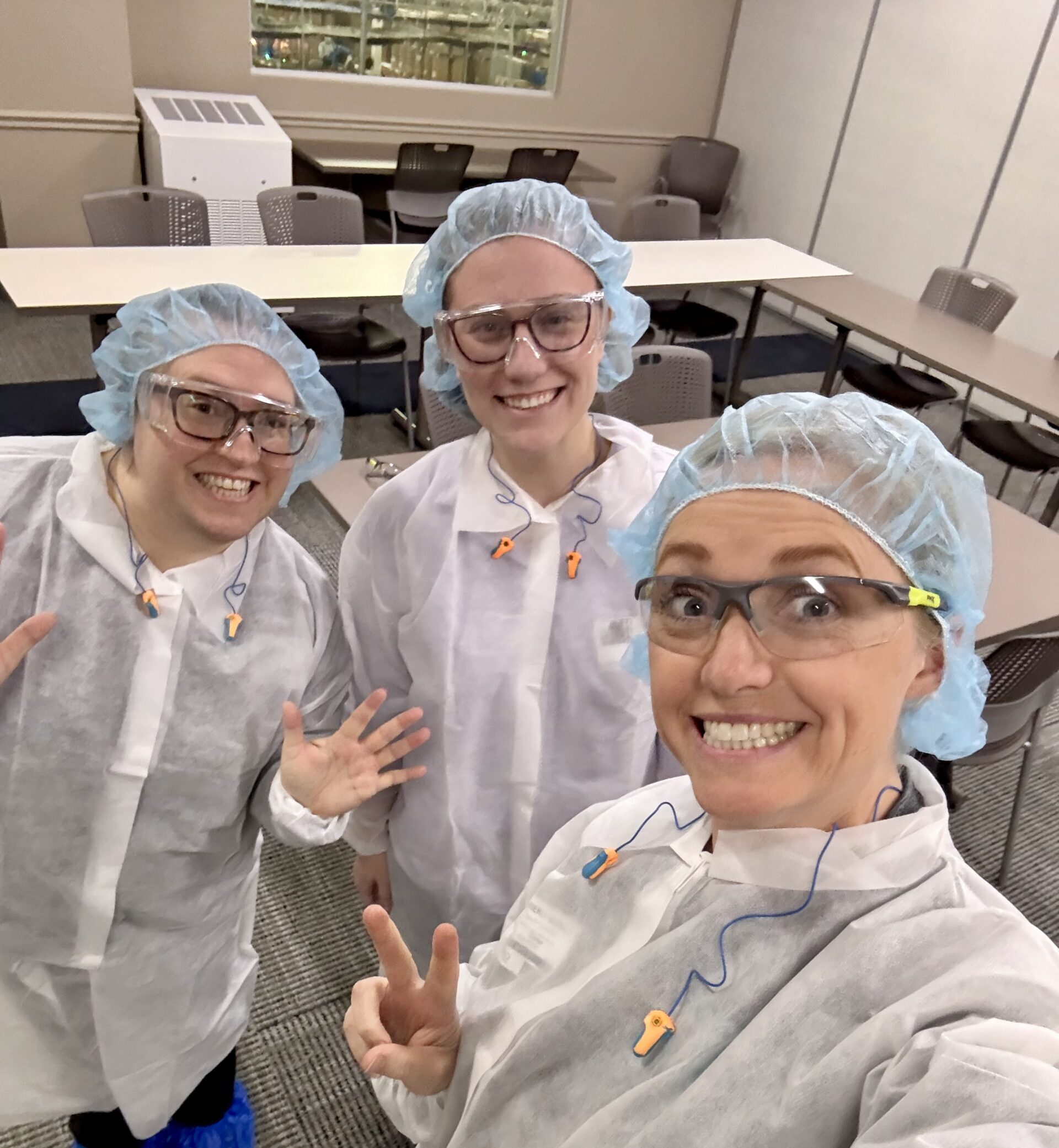 Three Crazy Richards employees in lab coats, hair nets, and safety glasses in a factory.